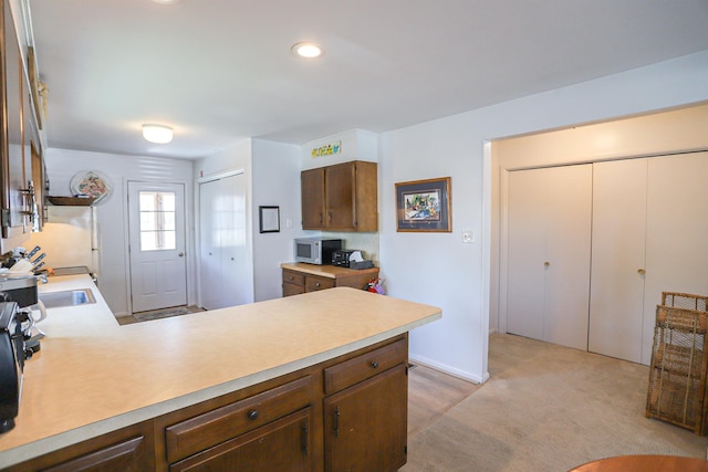 kitchen with kitchen peninsula, light carpet, and sink