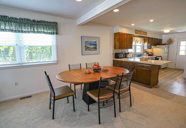 dining area featuring light colored carpet and beamed ceiling