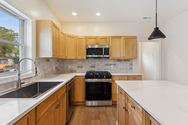 kitchen with backsplash, visible vents, appliances with stainless steel finishes, wood finished floors, and a sink