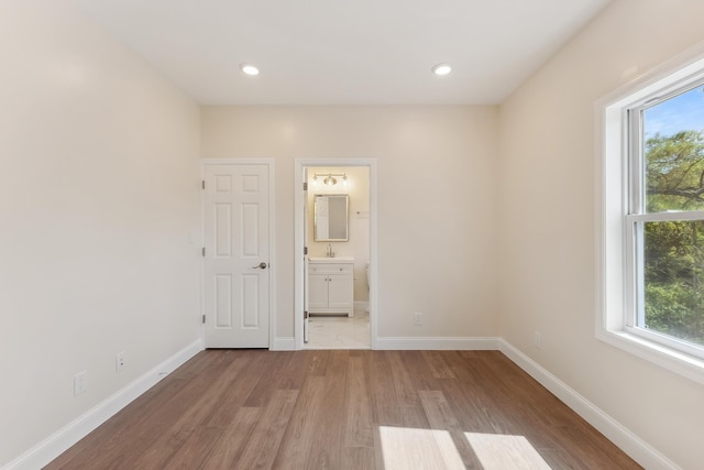 unfurnished bedroom with baseboards, a sink, light wood finished floors, and multiple windows