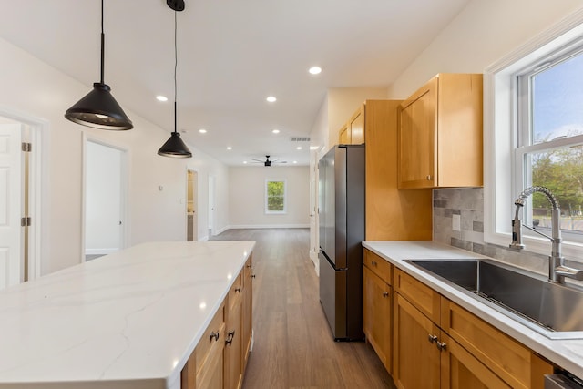 kitchen with freestanding refrigerator, wood finished floors, recessed lighting, a center island, and a sink