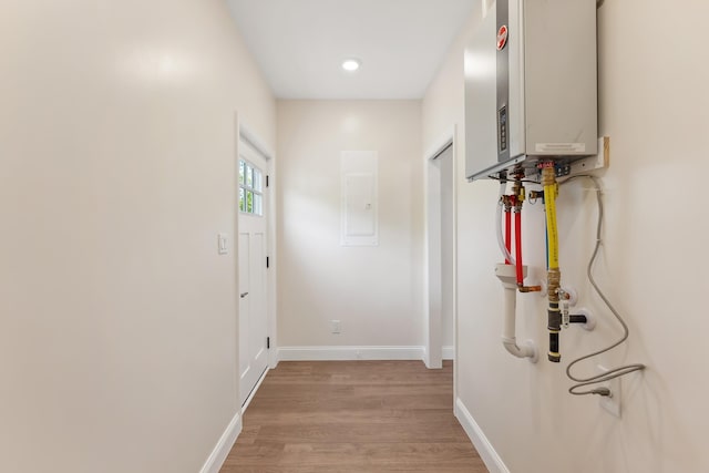 hallway with light wood-style floors, baseboards, recessed lighting, electric panel, and water heater