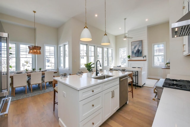 kitchen with light wood-type flooring, a sink, dishwasher, open floor plan, and a kitchen bar