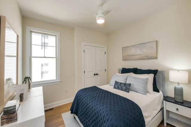 bedroom featuring wood finished floors, visible vents, baseboards, ceiling fan, and a closet