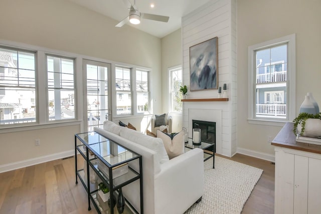 living area featuring a fireplace, wood finished floors, baseboards, and ceiling fan