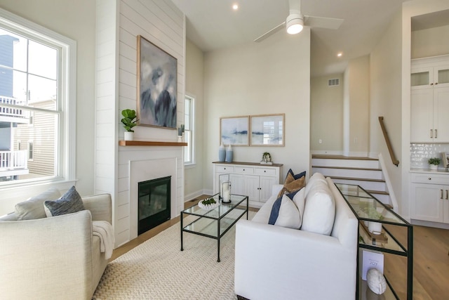 living room featuring visible vents, a large fireplace, ceiling fan, stairs, and wood finished floors