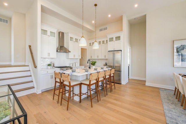 kitchen featuring visible vents, light wood-style flooring, a kitchen breakfast bar, wall chimney exhaust hood, and high quality fridge