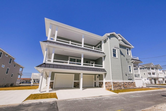 view of front of property featuring driveway, a standing seam roof, stone siding, an attached garage, and metal roof