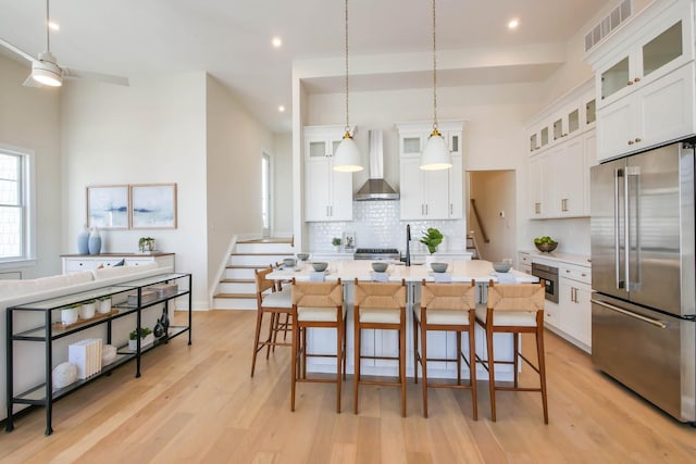 kitchen featuring visible vents, light wood finished floors, high end refrigerator, wall chimney exhaust hood, and tasteful backsplash