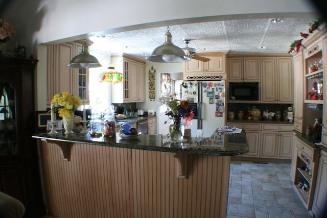 kitchen with a kitchen bar, kitchen peninsula, black microwave, white refrigerator, and hanging light fixtures