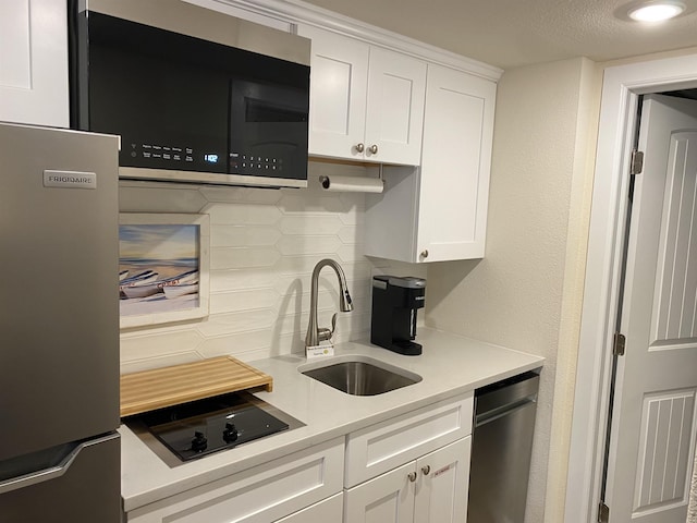 kitchen featuring stainless steel appliances, a sink, white cabinets, light countertops, and backsplash