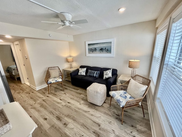 living area with a textured ceiling, wood finished floors, a ceiling fan, and baseboards