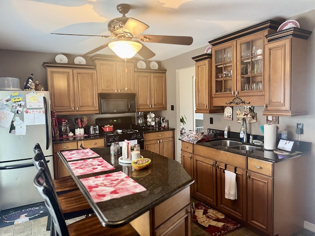 kitchen featuring ceiling fan, glass insert cabinets, a center island, black appliances, and a sink