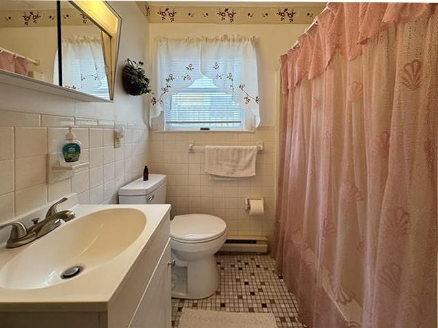 bathroom featuring tile walls, vanity, baseboard heating, toilet, and tile patterned floors