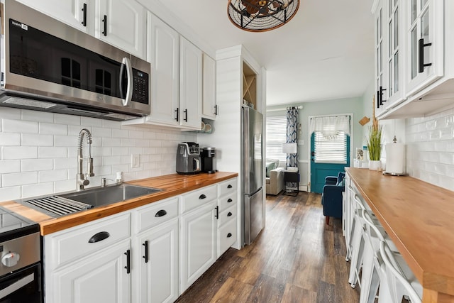 kitchen with appliances with stainless steel finishes, wooden counters, white cabinets, sink, and dark hardwood / wood-style floors