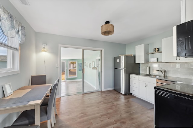 kitchen featuring light wood-type flooring, range with electric cooktop, sink, white cabinets, and stainless steel refrigerator