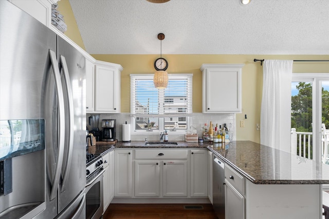 kitchen with decorative backsplash, appliances with stainless steel finishes, white cabinets, vaulted ceiling, and a peninsula