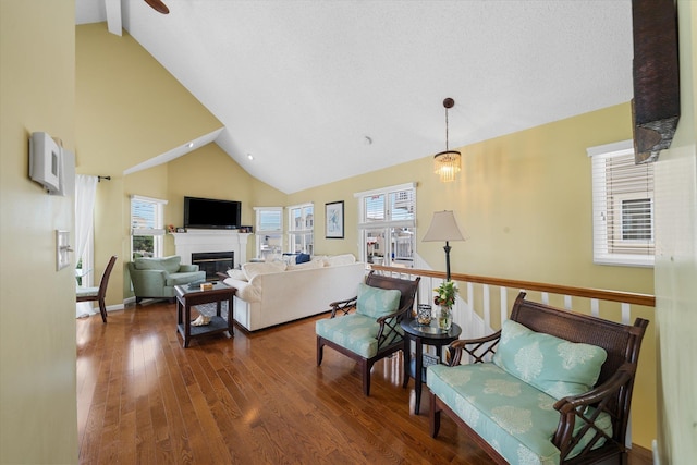 living area with baseboards, a glass covered fireplace, ceiling fan, wood finished floors, and high vaulted ceiling