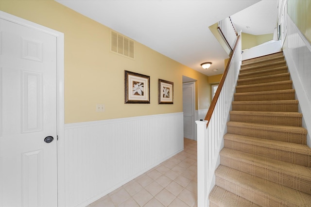 stairs with a wainscoted wall, tile patterned flooring, and visible vents