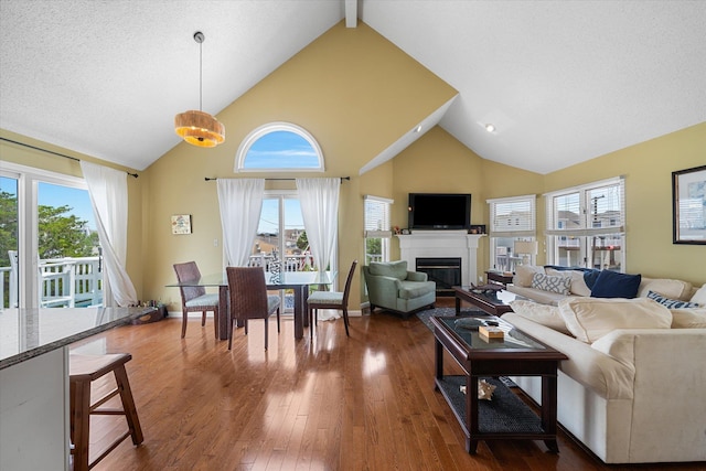 living area with dark wood-style floors, a glass covered fireplace, high vaulted ceiling, beamed ceiling, and baseboards