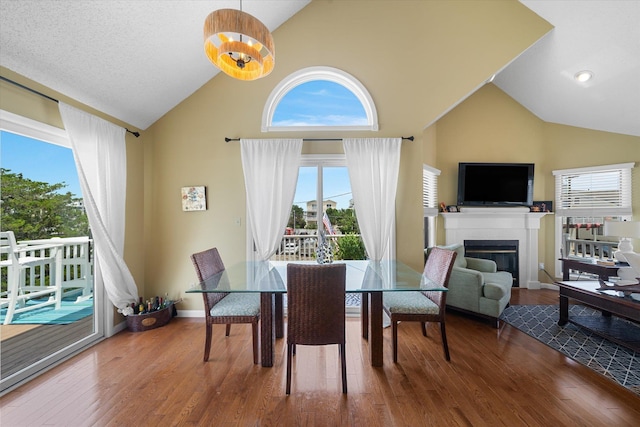 dining room with high vaulted ceiling, a glass covered fireplace, wood finished floors, and baseboards