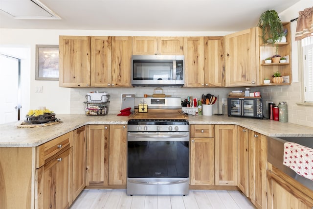 kitchen featuring a peninsula, light wood-type flooring, tasteful backsplash, light stone counters, and stainless steel appliances