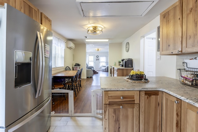 kitchen featuring brown cabinets, stainless steel fridge with ice dispenser, light stone counters, an AC wall unit, and open floor plan