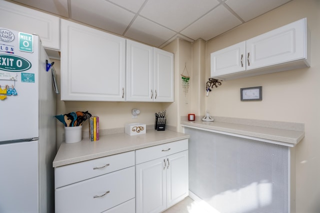 kitchen featuring freestanding refrigerator, white cabinets, light countertops, and a drop ceiling