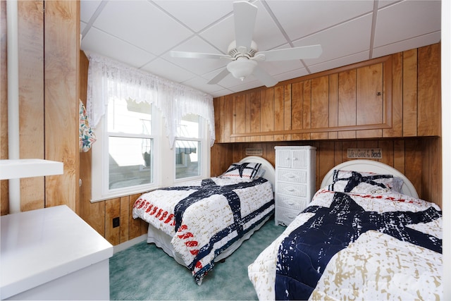 carpeted bedroom featuring a paneled ceiling, wooden walls, and a ceiling fan