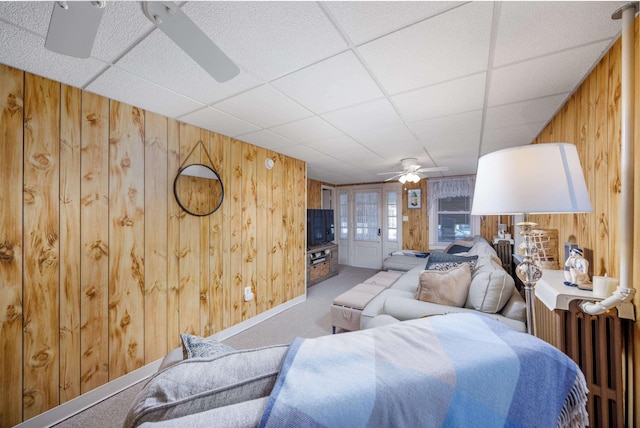 living room with wooden walls, a paneled ceiling, radiator heating unit, ceiling fan, and carpet floors