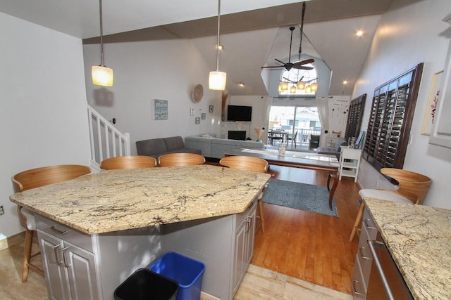 kitchen featuring ceiling fan, a center island, light stone countertops, a kitchen breakfast bar, and decorative light fixtures