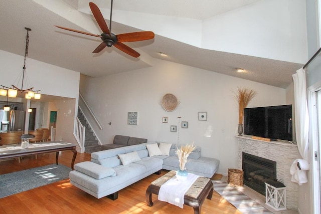 living room featuring ceiling fan with notable chandelier, wood-type flooring, a fireplace, and high vaulted ceiling