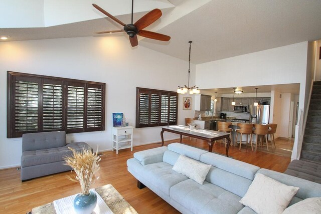 living room featuring ceiling fan with notable chandelier, light wood-type flooring, and high vaulted ceiling