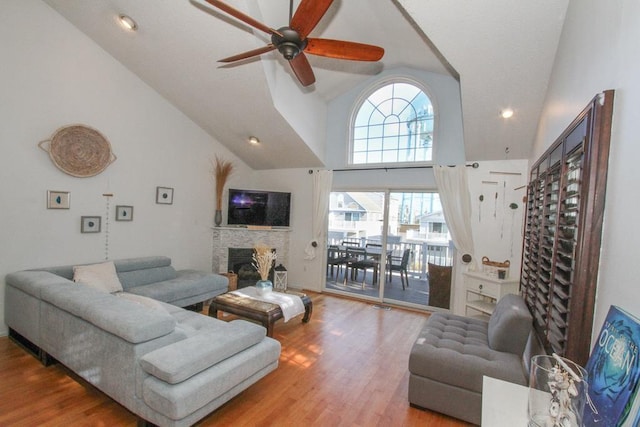 living room with a stone fireplace, ceiling fan, high vaulted ceiling, and hardwood / wood-style flooring