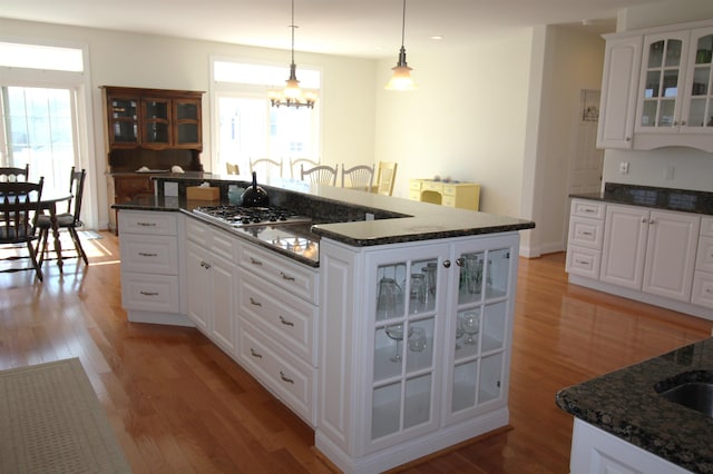 kitchen with white cabinetry, hanging light fixtures, a kitchen island, and dark stone countertops