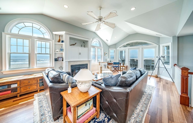 living room with light wood-style floors, a glass covered fireplace, vaulted ceiling, and a ceiling fan