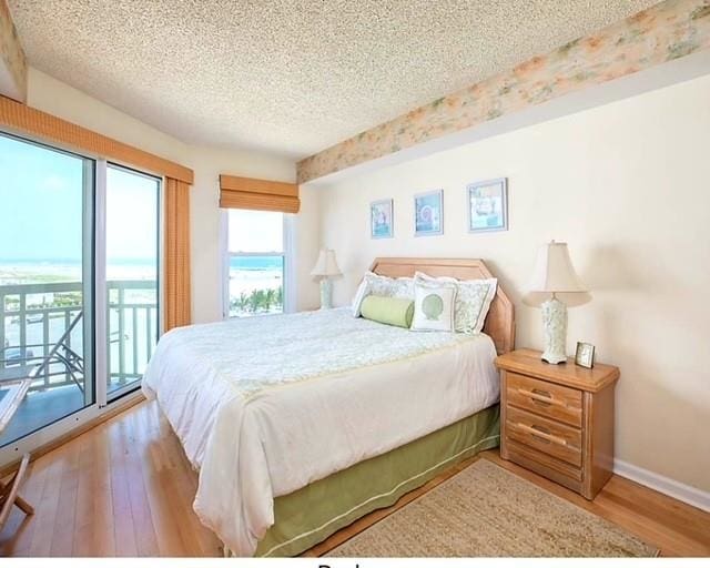 bedroom with access to exterior, hardwood / wood-style floors, and a textured ceiling