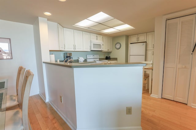 kitchen featuring light hardwood / wood-style flooring, white cabinets, white appliances, and kitchen peninsula