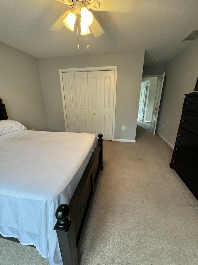 bedroom featuring ceiling fan, a closet, light colored carpet, and a textured ceiling