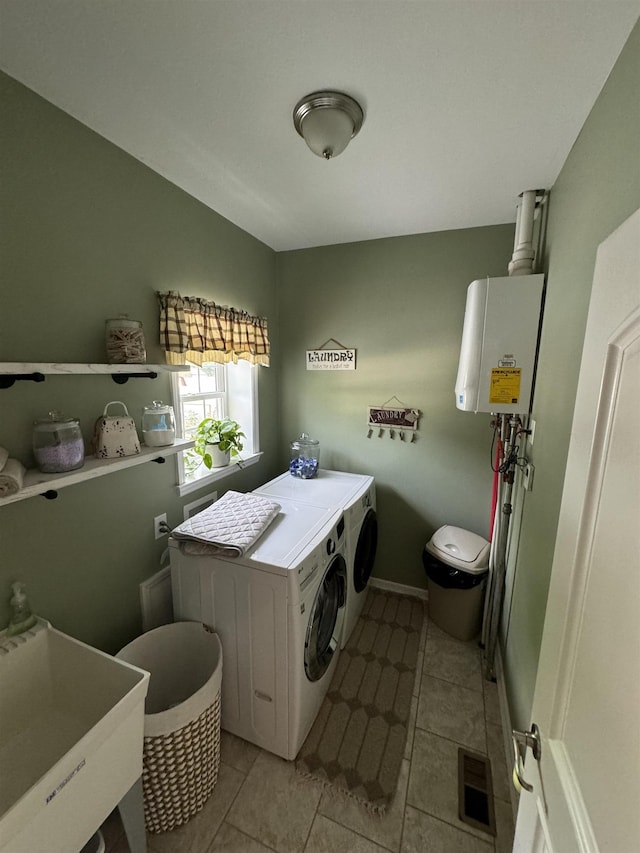 washroom featuring light tile patterned flooring, tankless water heater, washer and clothes dryer, and sink