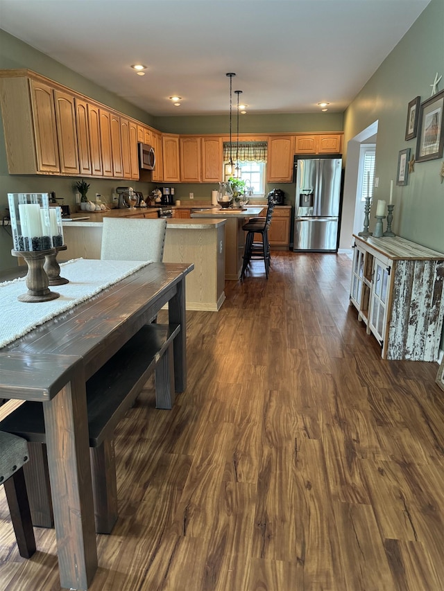 kitchen featuring appliances with stainless steel finishes, dark hardwood / wood-style flooring, decorative light fixtures, and a kitchen breakfast bar