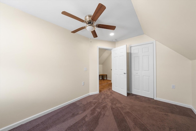 unfurnished bedroom featuring ceiling fan, a closet, dark carpet, and lofted ceiling