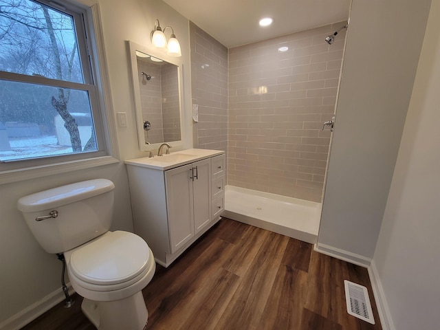 bathroom featuring vanity, tiled shower, hardwood / wood-style floors, and toilet