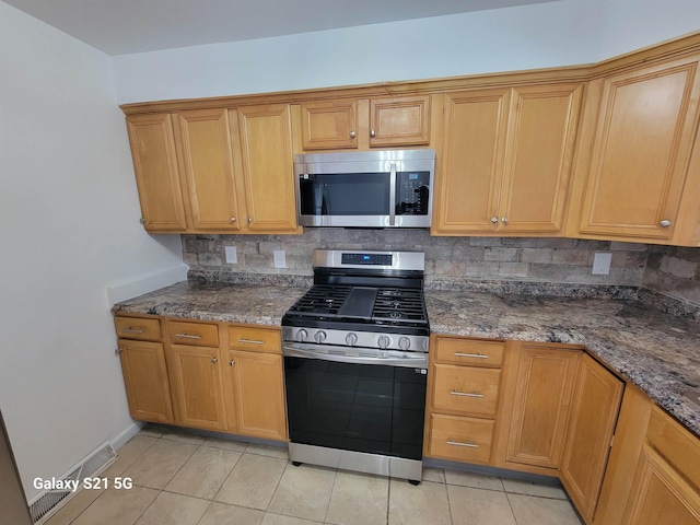 kitchen with backsplash, appliances with stainless steel finishes, light tile patterned floors, and dark stone counters