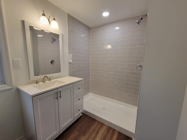 bathroom with wood-type flooring, tiled shower, and vanity