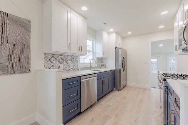 kitchen with stainless steel appliances, a sink, visible vents, white cabinets, and backsplash