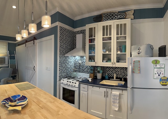 kitchen with a barn door, a sink, white appliances, wall chimney exhaust hood, and ornamental molding