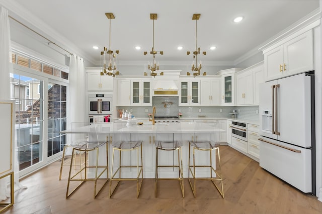 kitchen featuring white appliances, light countertops, custom range hood, white cabinetry, and a notable chandelier