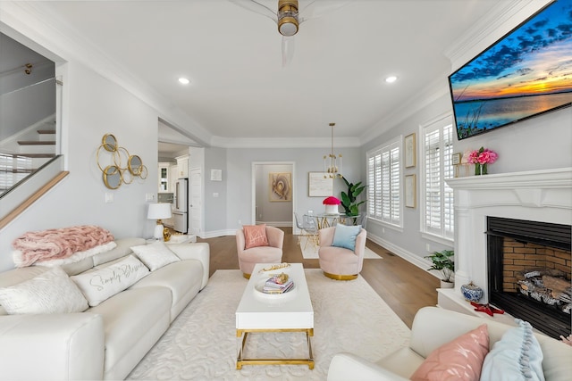 living area with stairway, wood finished floors, baseboards, a fireplace with raised hearth, and ornamental molding