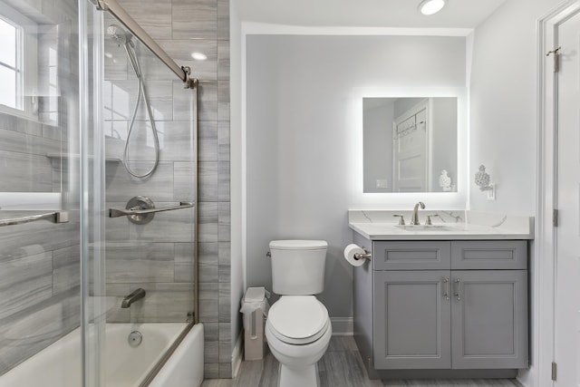 full bathroom featuring baseboards, toilet, wood finished floors, enclosed tub / shower combo, and vanity